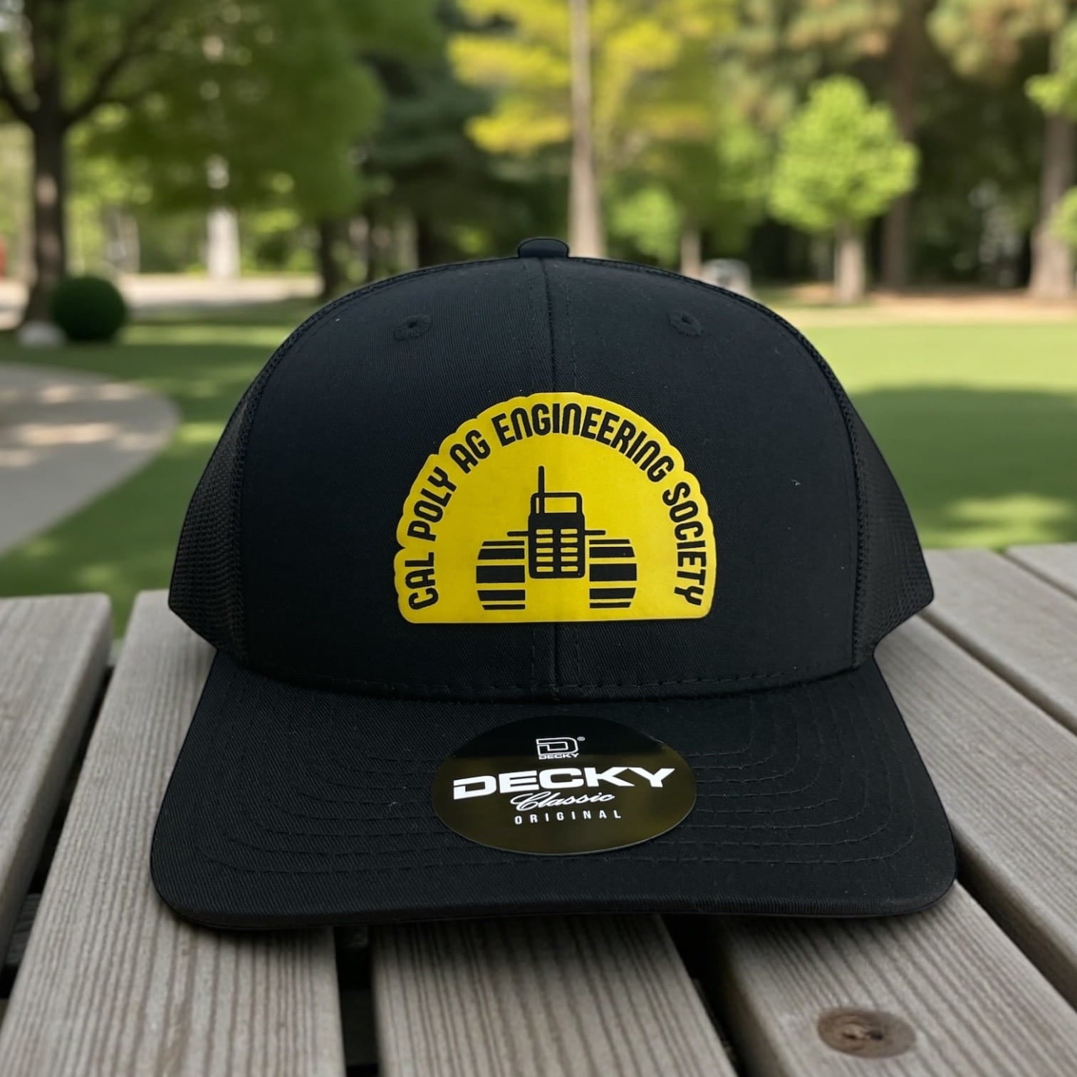 Black Decky trucker hat with yellow Cal Poly Ag Engineering Society logo and tractor icon on the front panel.