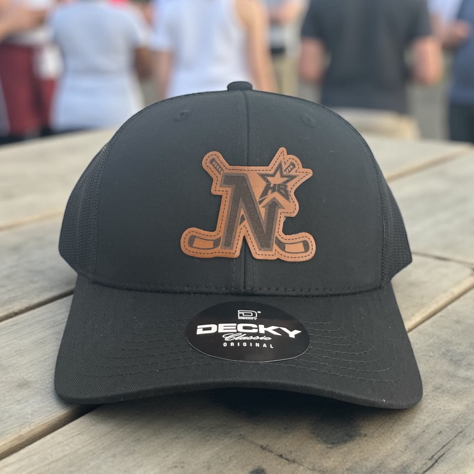 Black Decky trucker hat with tan leather patch featuring an N letter and star logo on the front panel.