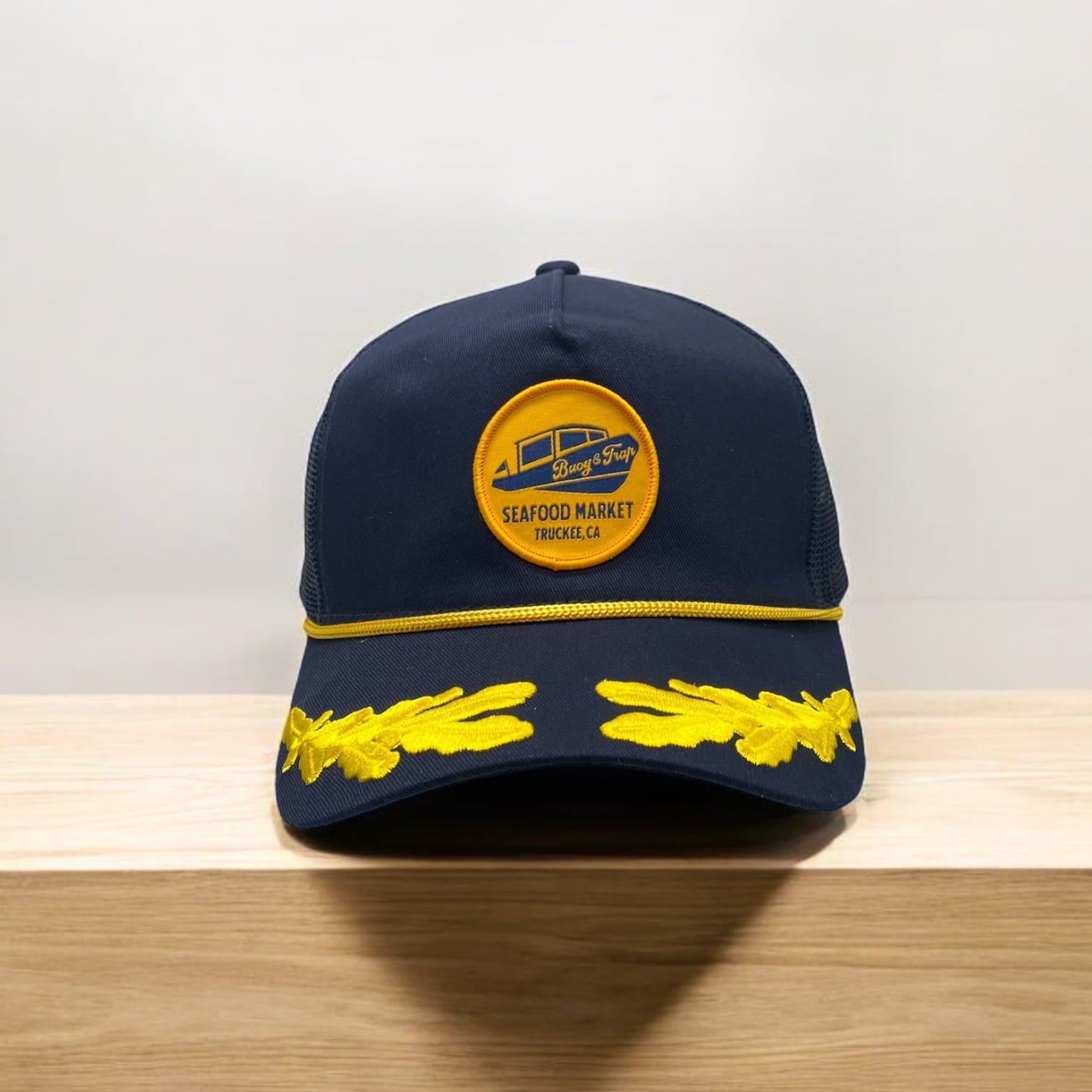 Navy rope trucker hat with yellow Buoy & Trap Seafood Market Truckee, CA patch and yellow leaf embroidery on brim.