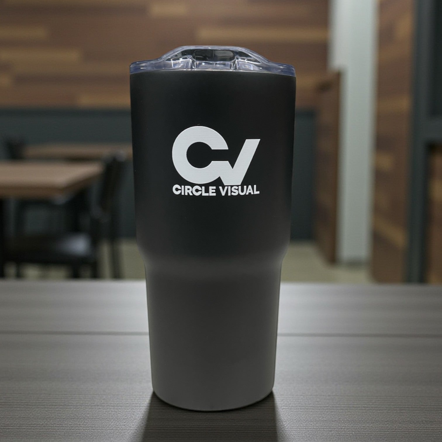 Black insulated tumbler with CV Circle Visual logo in white, clear lid, photographed on a table.