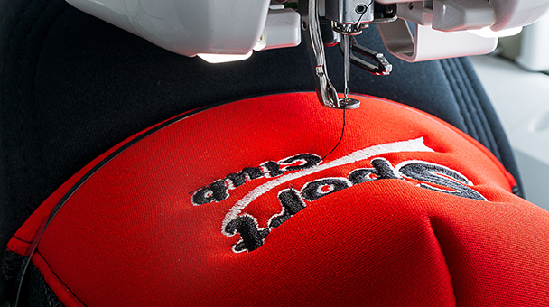 Close-up of a machine embroidering a white logo on a red cap.