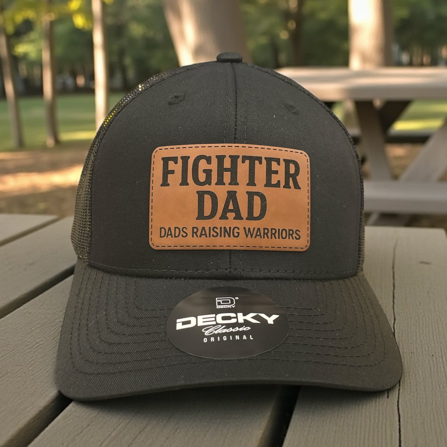 Black Decky trucker hat with brown “Fighter Dad” patch and “Dads Raising Warriors” text on the front panel.