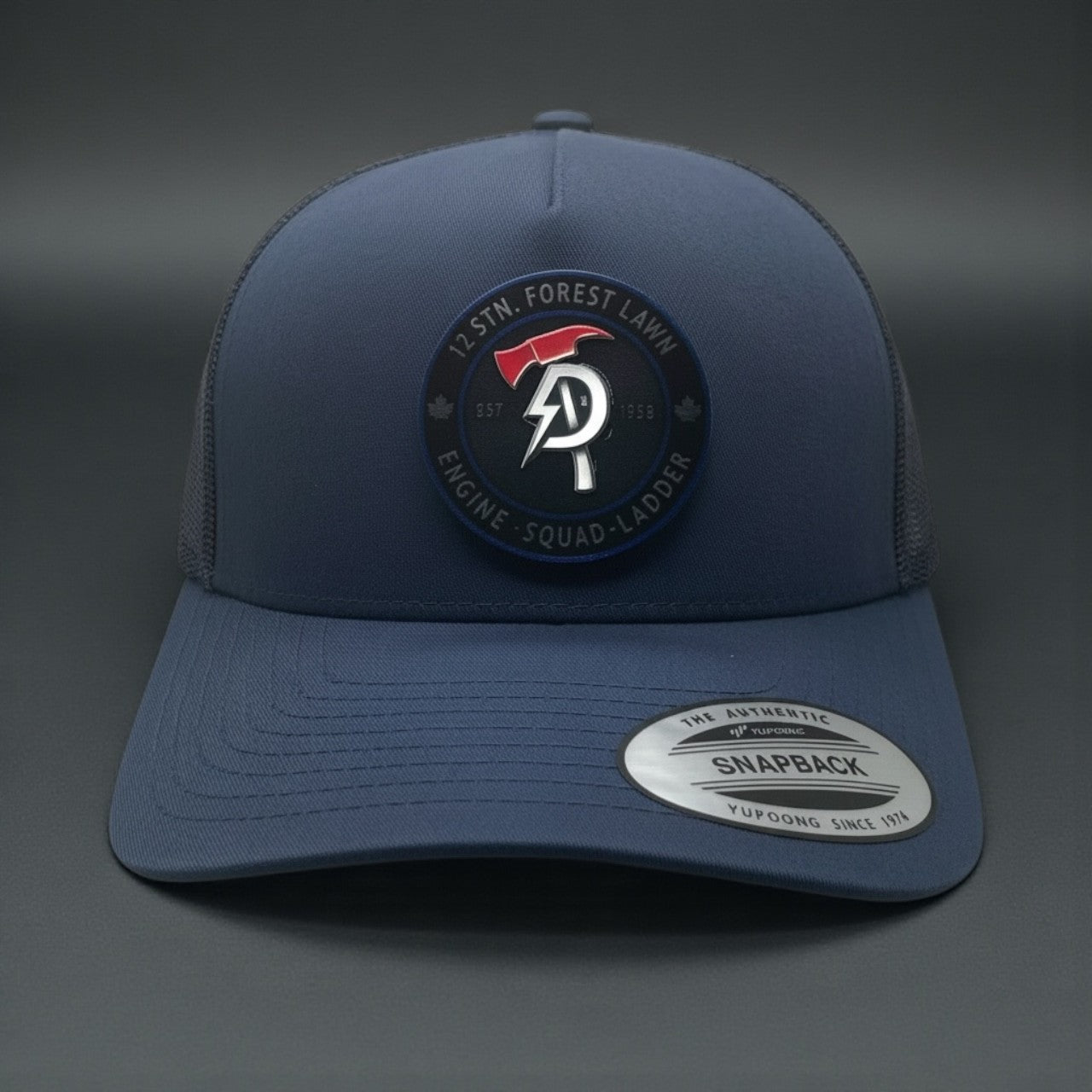 Navy Yupoong snapback hat with 12 Stn. Forest Lawn Engine-Squad-Ladder fire patch logo on the front.