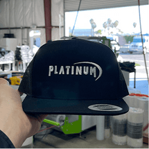 Black cap with 'PLATINUM' logo in a workshop.