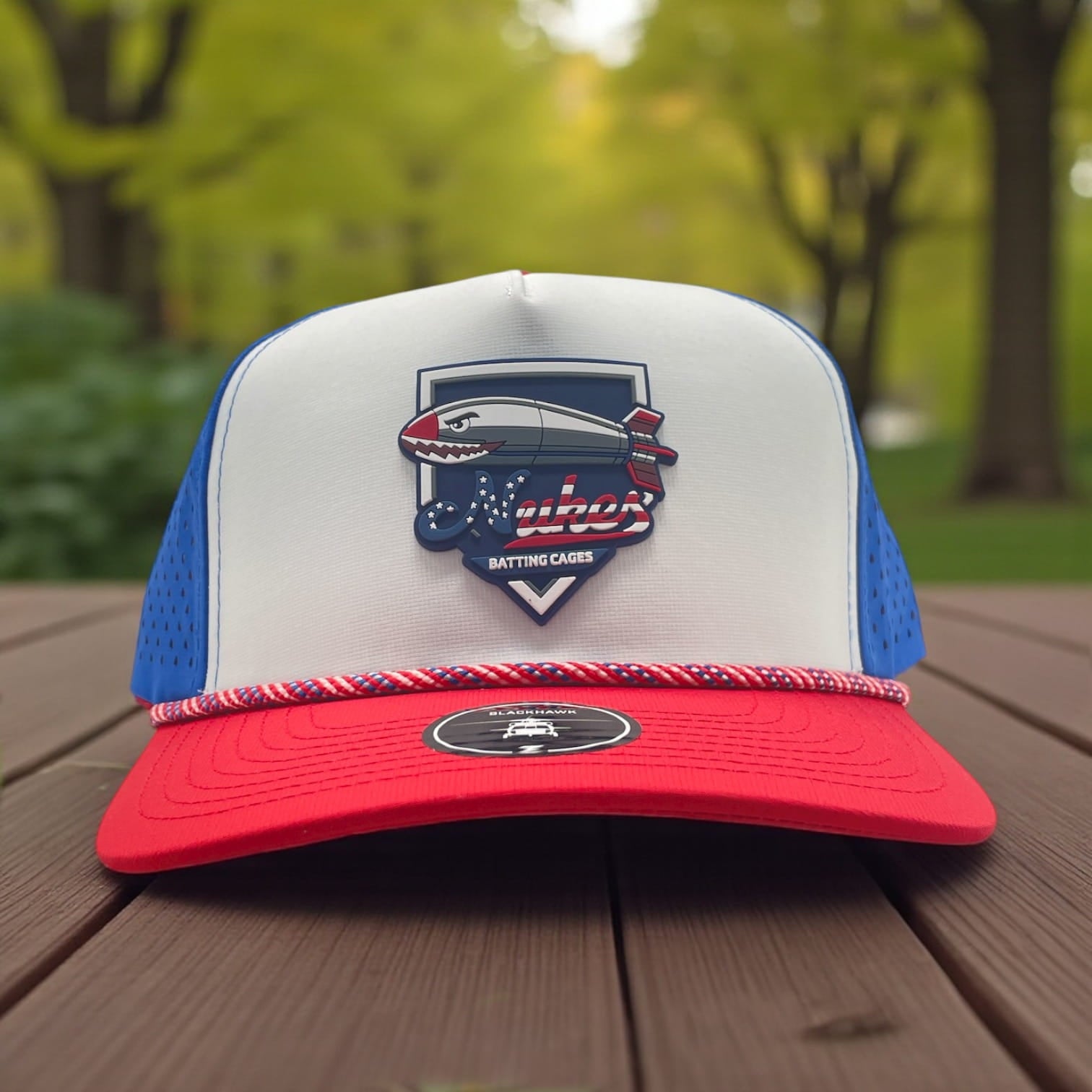Red, white and blue rope trucker hat with Nuker Batting Cages blimp logo patch on front.