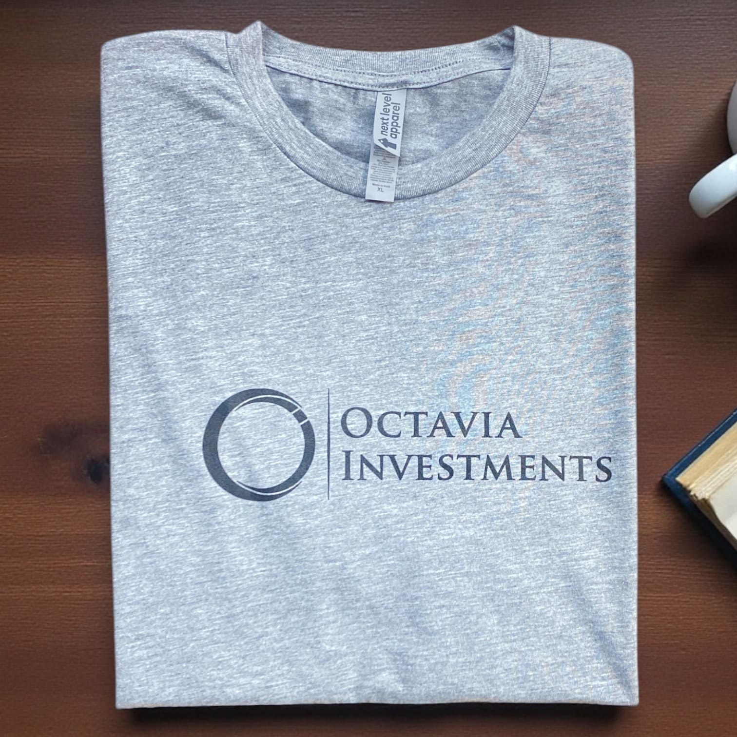 Heather gray Octavia Investments logo t-shirt folded on wooden desk, crewneck corporate apparel.