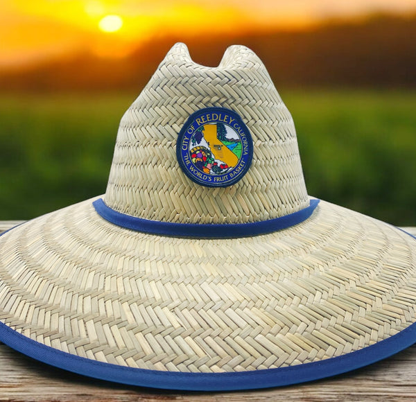 Wide-brim straw hat with City of Reedley California patch and blue trim, photographed at sunset