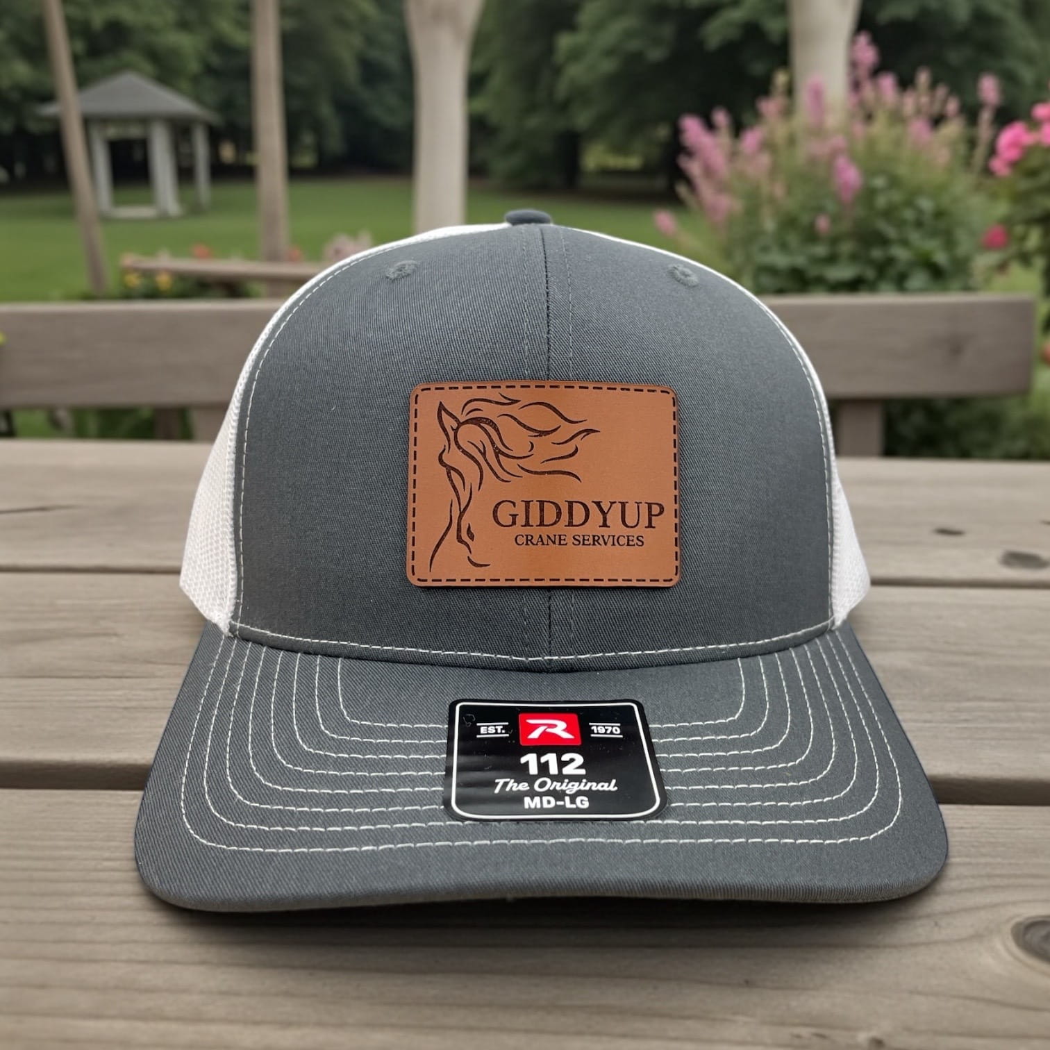 Gray and white Richardson 112 trucker hat with brown leather Giddyup Crane Services patch and horse head graphic.