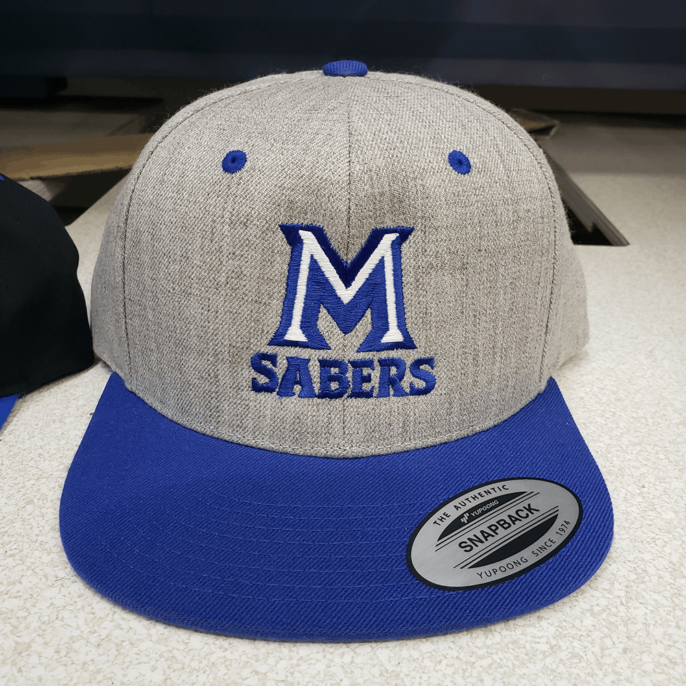 Heather gray and royal blue Yupoong snapback with embroidered M Sabers logo, flat bill, adjustable snap closure.
