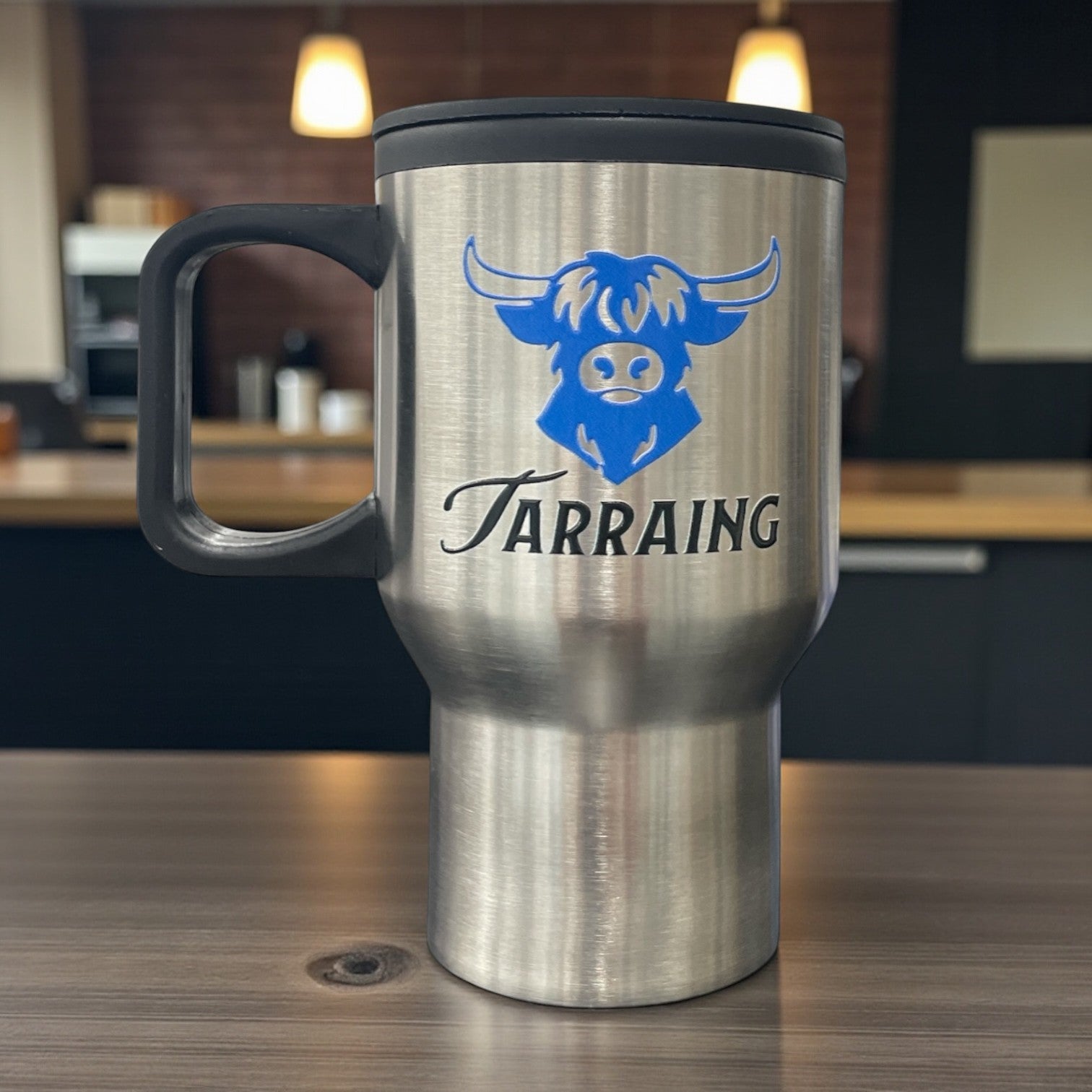 Stainless steel travel mug with handle featuring blue cow head logo and 'Tarraing' text on the front.